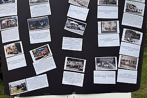 Schwarze Pinnwand mit mehreren Fotos und Texten, darunter ein weißes Schild mit roter Schrift 'Die Geschichte des Wohnhauses'