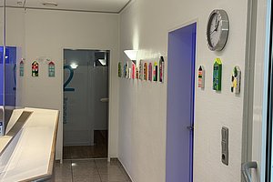 Flur mit blauen Türen, Wanduhren und bunten, haushaltsgegenständenähnlichen Dekorationen an der Wand