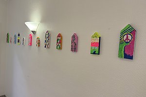 Wand mit einer Reihe kleiner, bunt bemalter Holzhausformen unter einer Wandlampe
