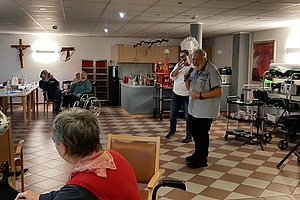Gesellige Veranstaltung in einem Raum mit Senioren, einem Sänger und festlicher Dekoration.