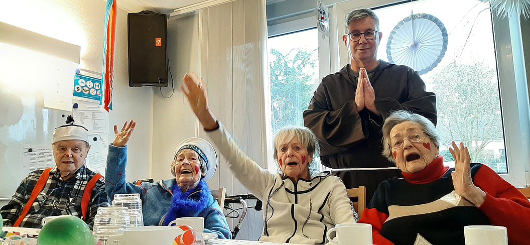 Gruppenfoto von älteren Menschen, die fröhlich die Hände heben, mit einem Mann im Hintergrund.